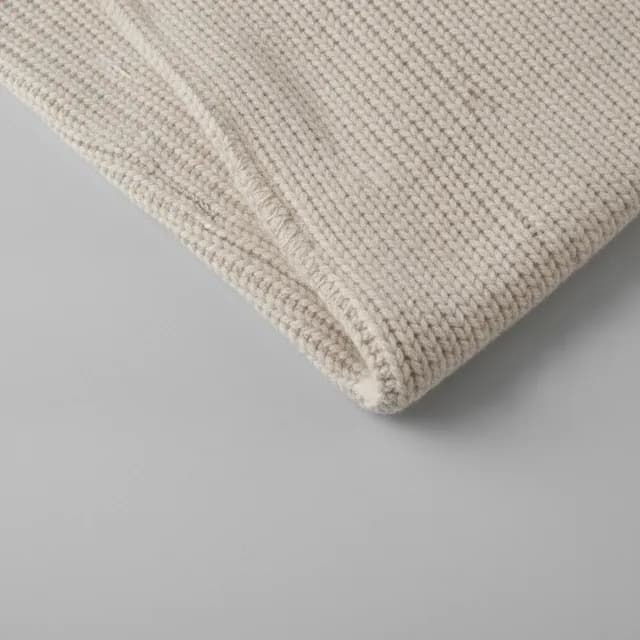 A close macro of the ribbed edge of a cream knitted blanket